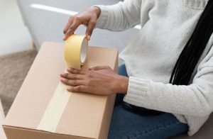 تصویری از یک فرد در حال بسته بندی یک محصول شکننده با استفاده از کارتن بسته بندی و چسب پهن